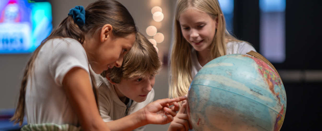 Three students looking and pointing at a globe in their classroom