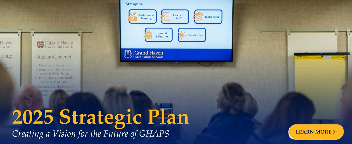 A group of strategic plan working group members viewing a screen displaying the strengths of Grand Haven Area Public Schools, with the text 2025 Strategic Plan: Creating a Vision for the Future of GHAPS
