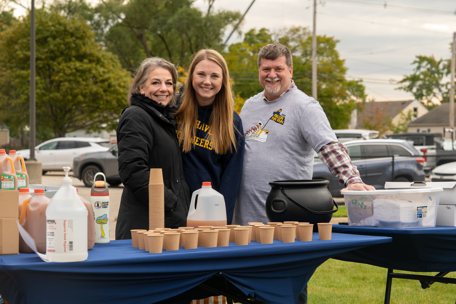 Three parent volunteers smiling while they serve apple cider during a school event.