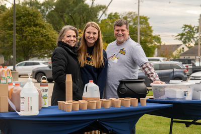Three parent volunteers smiling while they serve apple cider during a school event.