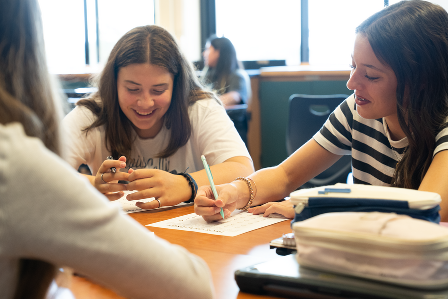 Two middle school girls smiling at each other while working together at a classroom table.