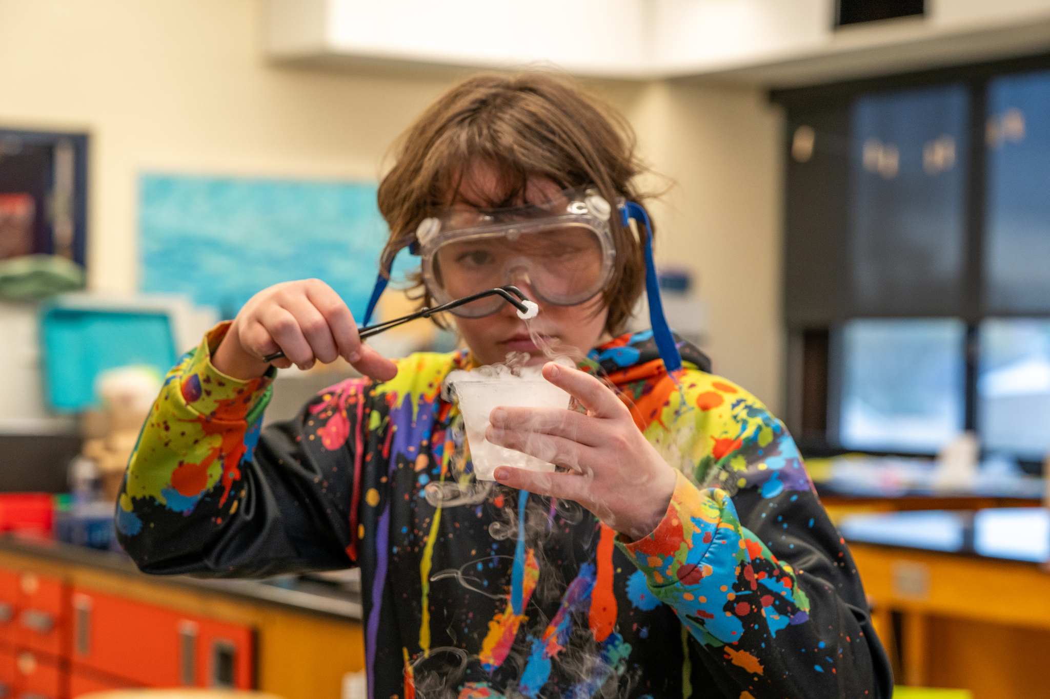A student looking closely at a cup with dry ice through a pair of goggles in science class