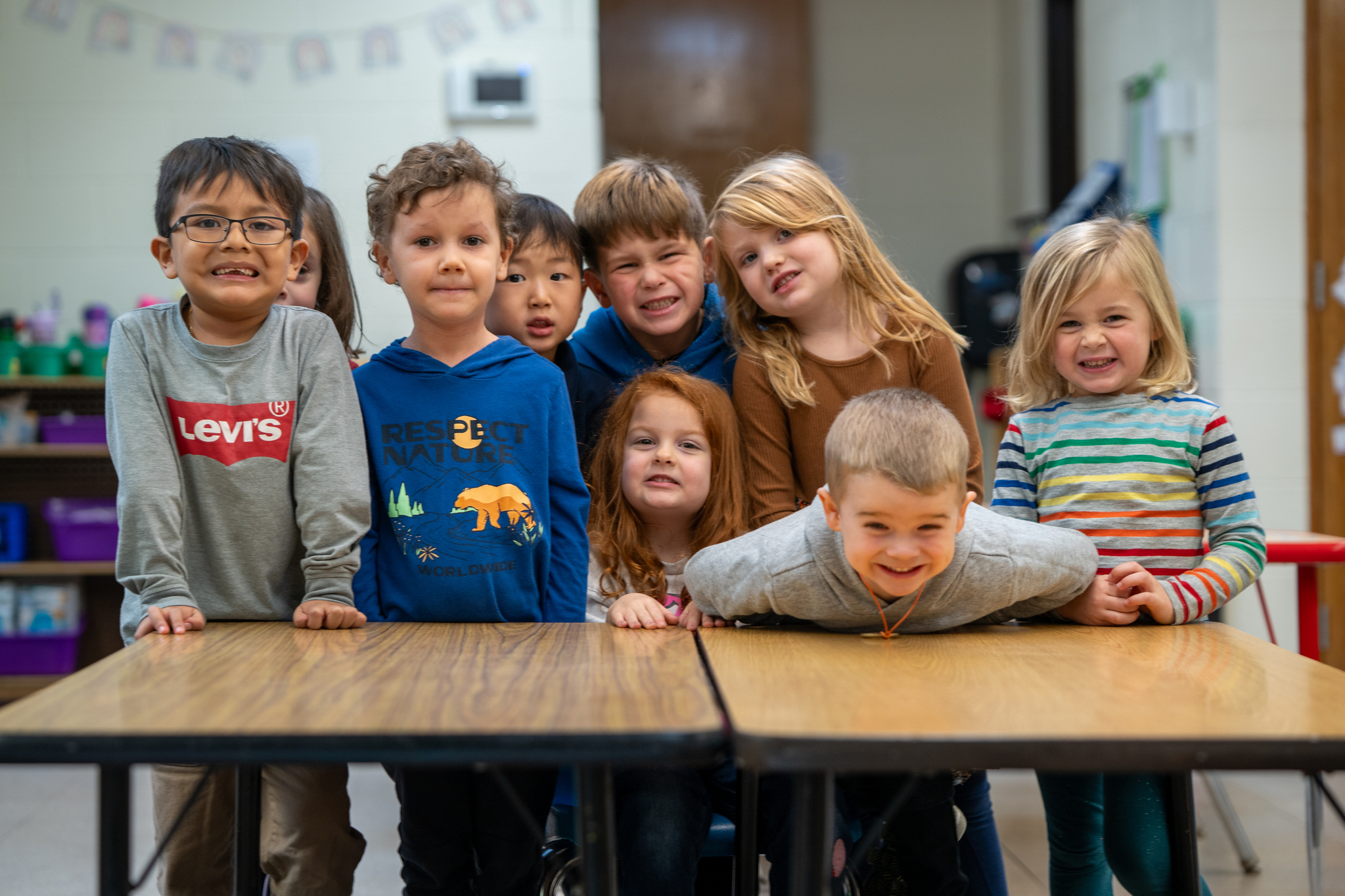 Preschoolers huddled around a table in a classroom, smiling and being goofy