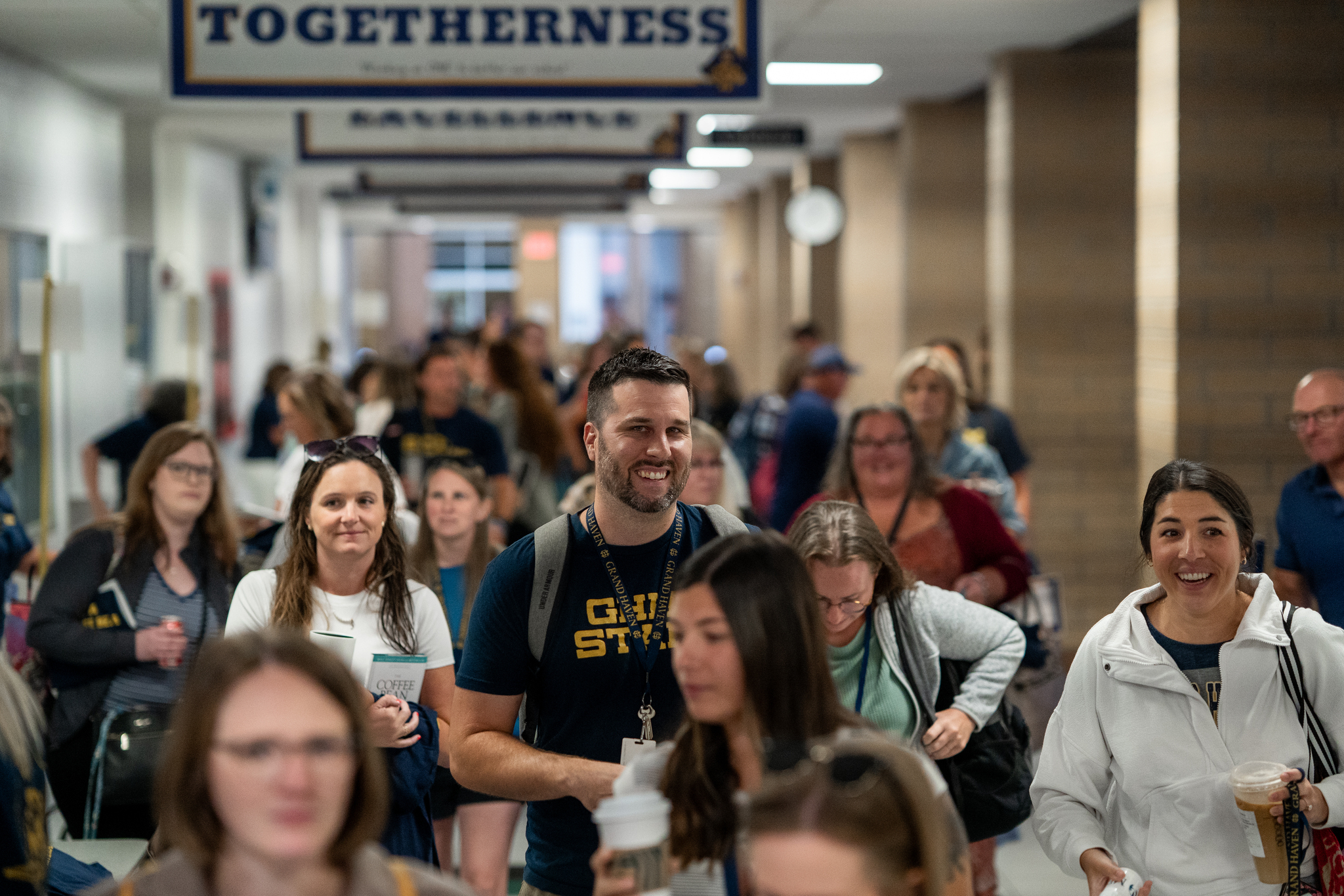 A large group of smiling teachers walking down the halls of Grand Haven High School.