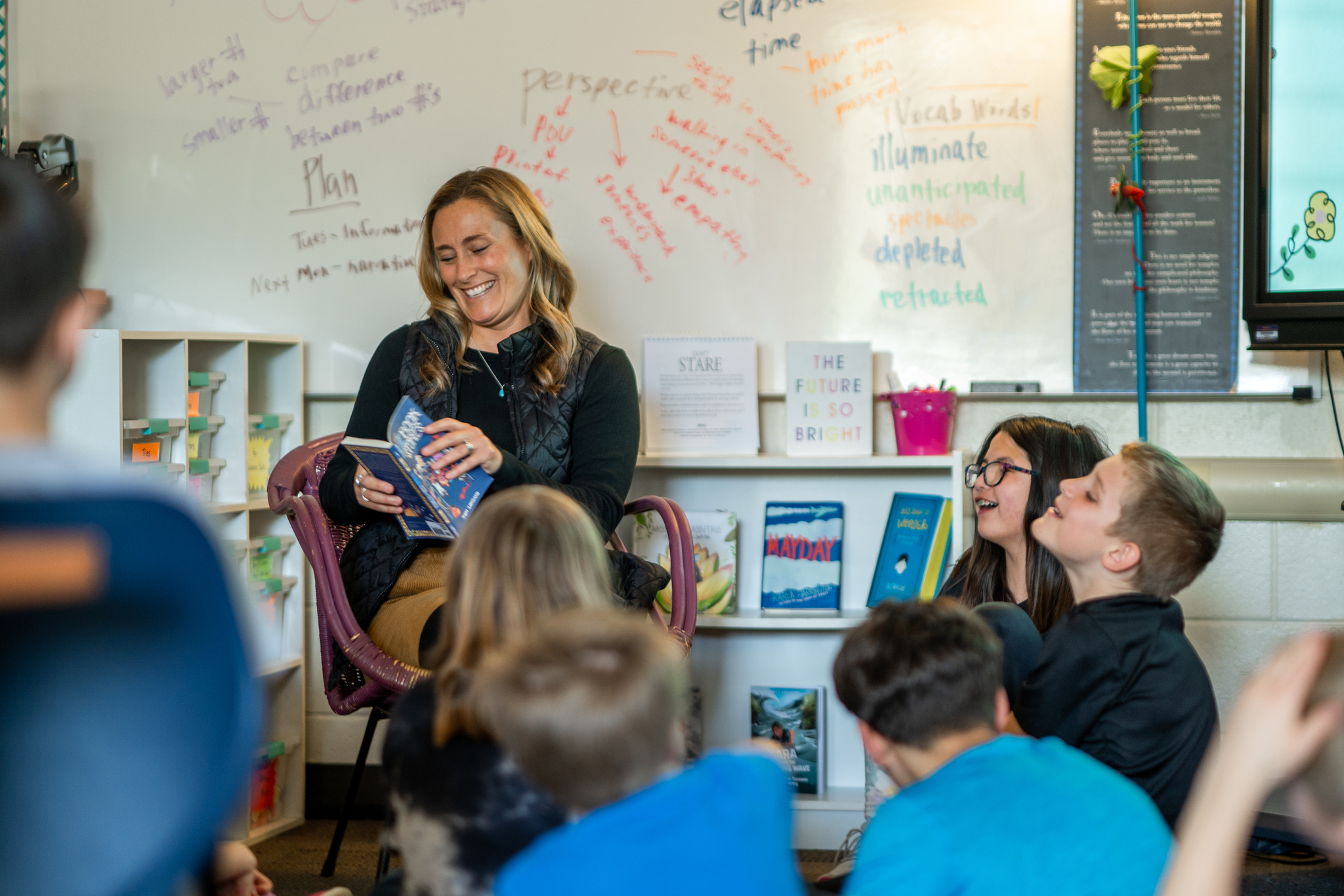 A teacher smiling and reading a book to a class