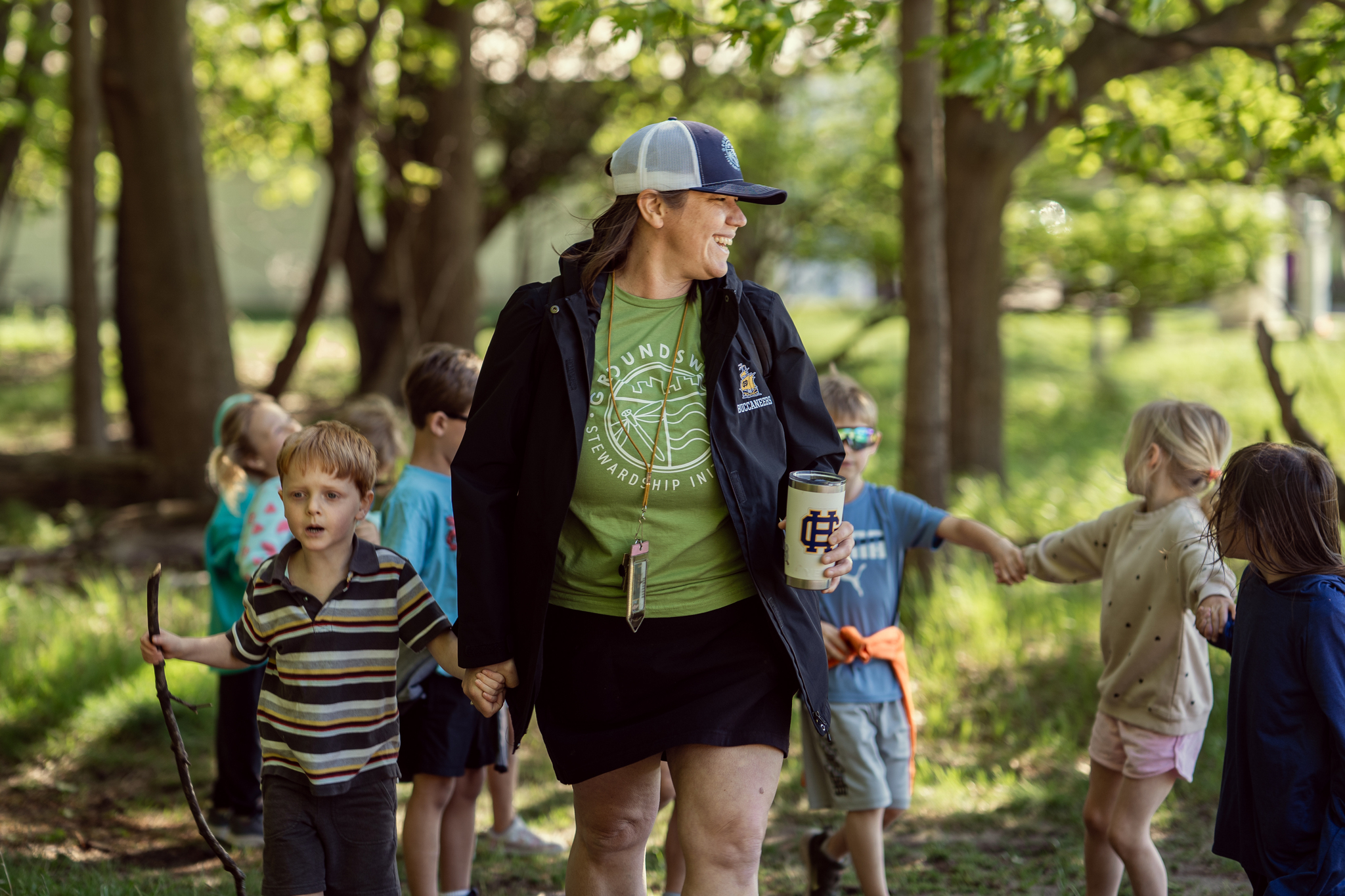 A teacher walking through the woods with a class of young children.