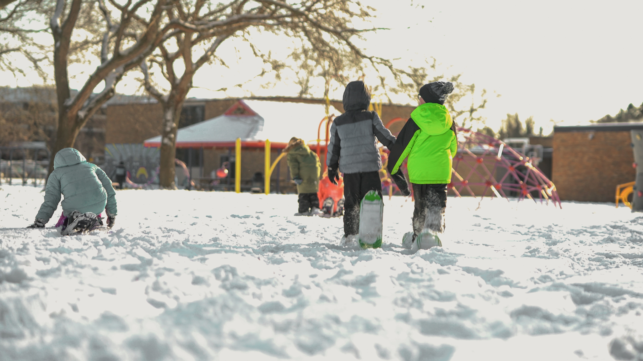 Students walking on a snowy playground, dressed up in their winter gear.