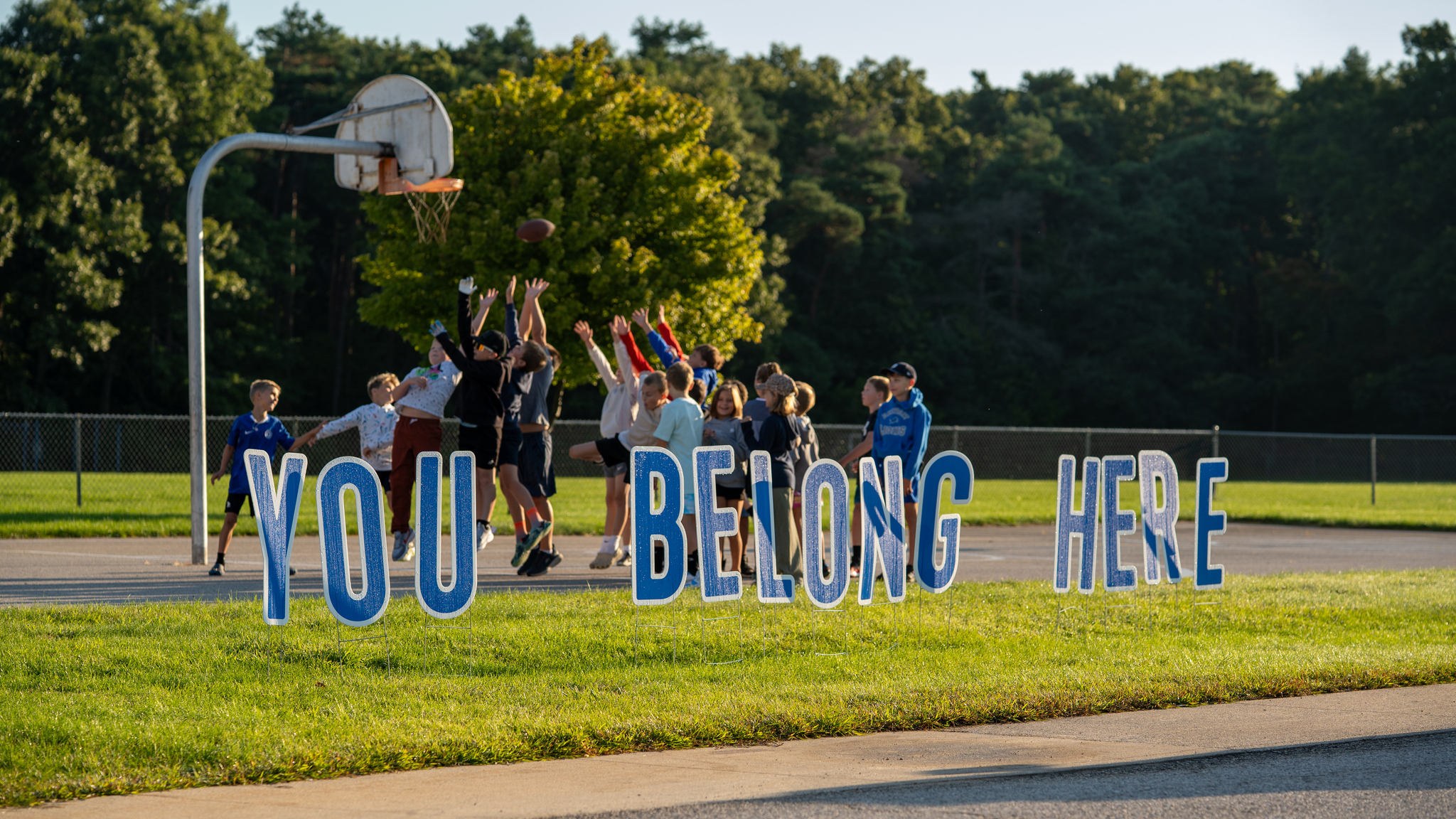 Students jumping to catch a football behind a sign that says YOU BELONG HERE